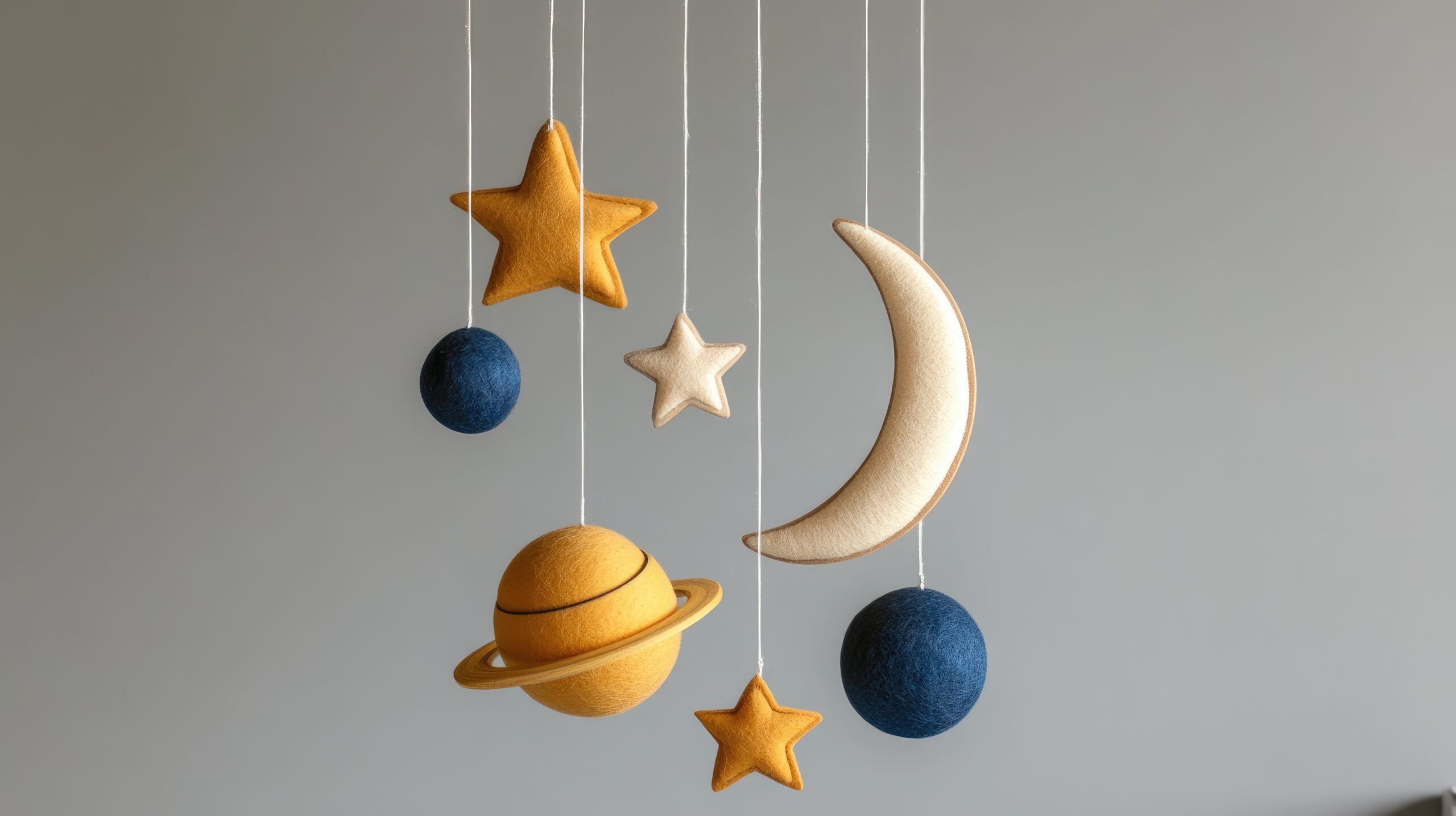 Handmade baby mobile featuring stars planets and a moon crafted from eco friendly felt and wood suspended above a crib on a gray backdrop