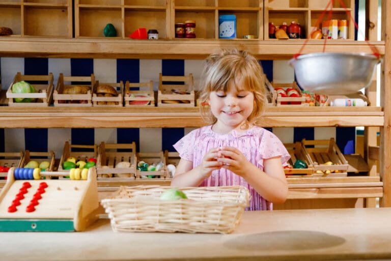 Little preschool girl play with food and grocery wooden toys. Happy active child playing role game as cashier or seller, in wood shop or supermarket. Education, activity for kids